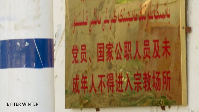 This Jummah mosque is in Shazaojing village of the Huicheng township in Kumul. The crescent moon and star symbols on top of the mosque have all been removed, and tight wire netting has been attached to the surrounding walls. The notice at the entrance reads: “Party members, state officials, and minors not allowed in religious establishments.”