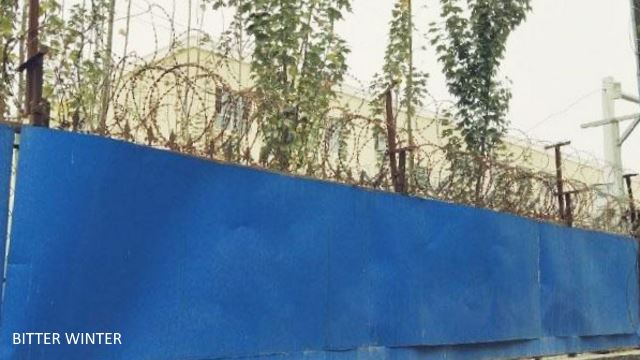 The outer wall is covered with blue steel plates. The top of the wall has been fitted with spiral-shaped barbed wire.