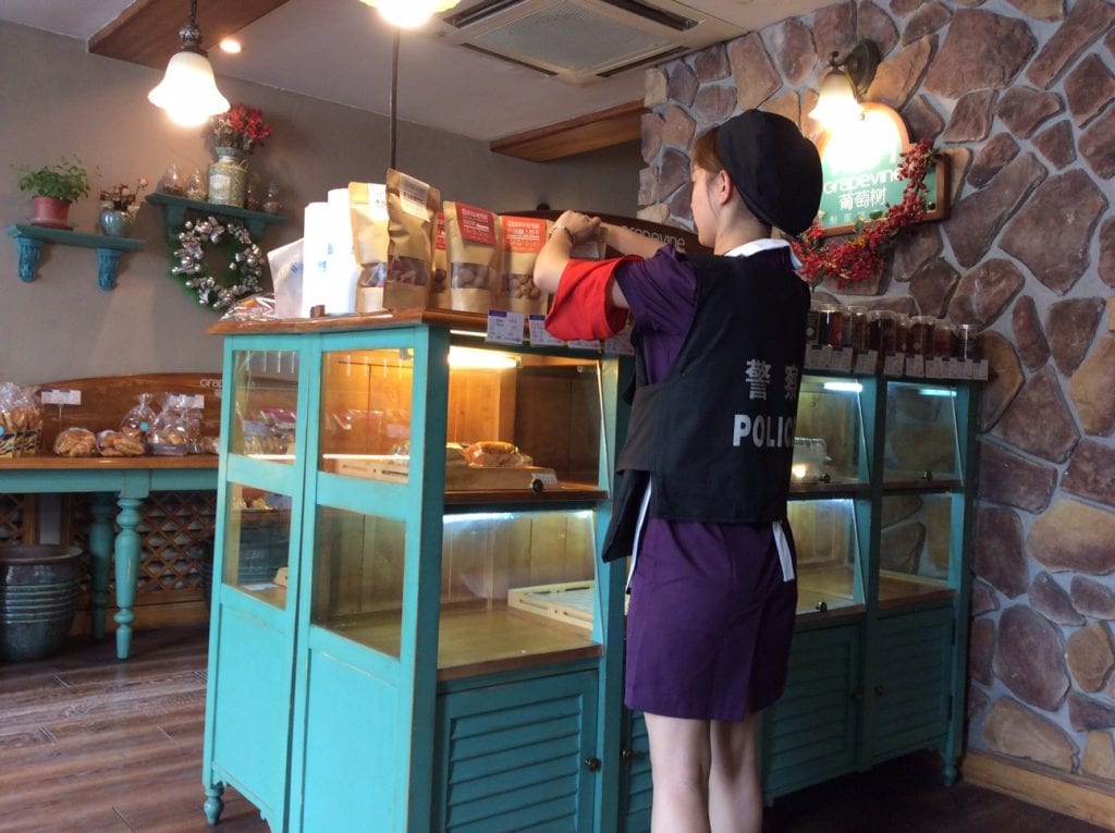 Everyone is drafted into the war on terror, even this young shop assistant, wearing her compulsory red armband and bullet proof vest. Summer 2017.