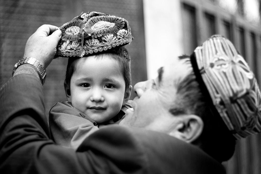 A man put an embroidered doppa (the traditional cap) on his son.