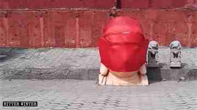 The head of a demolished Buddha statue is wrapped in red cloth.