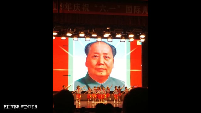 Children at a “red” performance, staged in front of the portrait of Mao Zedong.