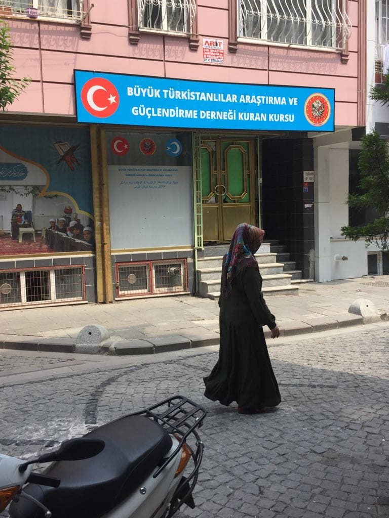 A Uyghur woman walks past a small madrasah